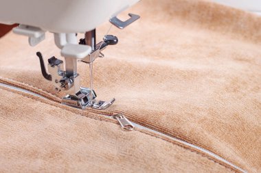 Modern dikiş makinesi bej kumaşlı, iplikli, özel presser ayaklı, yakın plan. Fermuara dikiş dikme işlemi. İş, hobi, el yapımı, sıfır atık, geri dönüşüm, tamir konsepti.