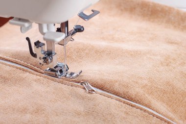 Modern sewing machine special presser foot with beige fabric and thread, closeup. Sewing process of sewing on a zipper. Business, hobby, handmade, zero waste, recycling, repair concept. clipart