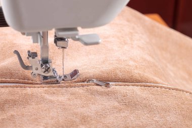 Modern dikiş makinesi, bej kadife kumaş ve iplikle özel presser ayak, yakın plan. Fermuara dikiş dikme işlemi. İş, hobi, el yapımı, sıfır atık, geri dönüşüm, tamir konsepti.