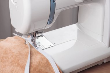 Modern dikiş makinesi, bej kadife kumaş ve iplikle özel presser ayak, yakın plan. Fermuara dikiş dikme işlemi. İş, hobi, el yapımı, sıfır atık, geri dönüşüm, tamir konsepti.
