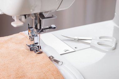 Modern dikiş makinesi, bej kadife kumaş ve iplikle özel presser ayak, yakın plan. Fermuara dikiş dikme işlemi. İş, hobi, el yapımı, sıfır atık, geri dönüşüm, tamir konsepti.