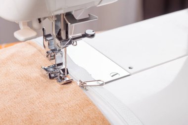 Modern dikiş makinesi, bej kadife kumaş ve iplikle özel presser ayak, yakın plan. Fermuara dikiş dikme işlemi. İş, hobi, el yapımı, sıfır atık, geri dönüşüm, tamir konsepti.
