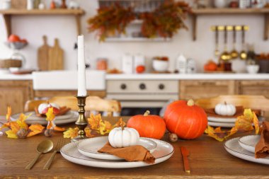 Yemek masası beyaz ve turuncu balkabaklarıyla, sonbahar yapraklarıyla ve mutfak arka planında şamdanla hazırlandı. Cadılar Bayramı için ev dekorasyonu, Şükran Günü ve sonbahar tatili..