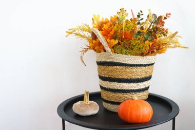 Siyah masanın üzerinde renkli sonbahar çiçekleriyle dolu dokuma sepet beyaz arka planda küçük balkabağı, odanın mevsimsel ambiyansını artırıyor. Sonbahar, Cadılar Bayramı, Şükran Günü ev dekorasyonu.