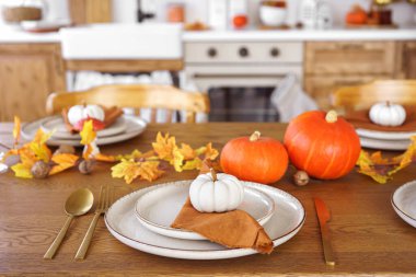 Yemek masası beyaz ve turuncu balkabaklarıyla, sonbahar yapraklarıyla ve mutfak arka planında şamdanla hazırlandı. Cadılar Bayramı için ev dekorasyonu, Şükran Günü ve sonbahar tatili..