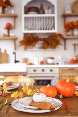 Yemek masası beyaz ve turuncu balkabaklarıyla, sonbahar yapraklarıyla ve mutfak arka planında şamdanla hazırlandı. Cadılar Bayramı için ev dekorasyonu, Şükran Günü ve sonbahar tatili..