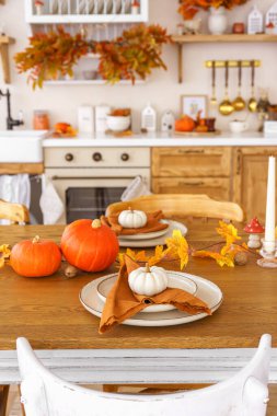 Yemek masası, sonbahar bayramları ya da Şükran Günü için şık bir set. Portakal kabakları, peçeteli tabaklar ve renkli yapraklarla, kırsal mutfakta sıcak ve davetkar bir atmosfer yaratıyor.
