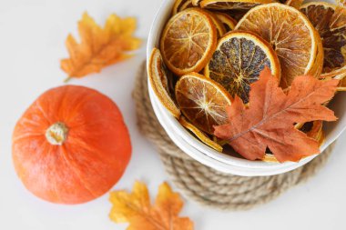 Kurumuş portakal dilimleri, turuncu balkabağı ve beyaz masa üstü yapraklı canlı sonbahar yapraklarıyla dolu beyaz kâse. Sağlıklı yiyecekler, doğal cips, üst manzara.
