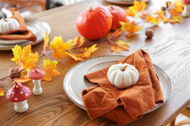 Beyaz ve turuncu balkabaklı güzel düzenlenmiş yemek masası, sonbahar sarısı yaprakları, kahverengi ahşap masa arkaplanındaki tabaklara katlanmış zarif peçeteler. Sonbahar tatilleri için ev dekorasyonu