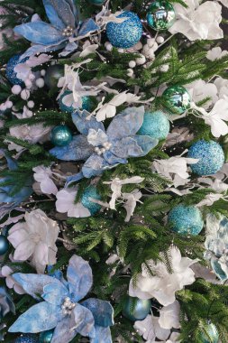 Mavi ve beyaz çiçeklerle süslenmiş Noel ağacı ışıklarla ve karlı dallarla süslenmiş. Kış tatili ve kutlamalar için mükemmel bir ortam. Duvar kağıdı, arkaplan, arkaplan