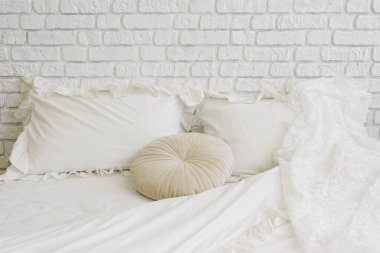 Sıcak beyaz yatak, beyaz tuğlalı arka planda yastıklı yatak. Yumuşak beyaz battaniyeli minimalist yatak, yumuşak yastık ve dikdörtgen yastıklar odada sıcak ve davetkar atmosfer yaratıyor..