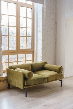 Sıcak yeşil haki rengi kadife kanepe. Parlak ve havadar bir yaşam alanı. Büyük pencereleri ve beyaz tuğlalı duvarları var. Modern tavan arası minimalist tasarımı. İç mekan, yaşam alanı, ev dekorasyonu.