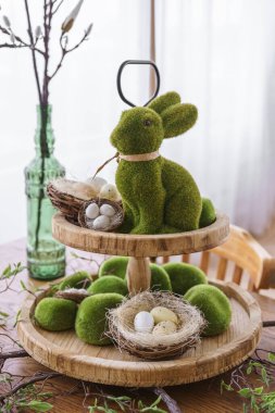 Yeşil yosun Paskalya Tavşanı ve dekoratif Paskalya yumurtaları yuvanın arka planında iki katlı ahşap tabakta. Bahar tatilleri için ev dekorasyonu, şenlik masası.