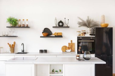 Tezgahı beyaz mutfak ve beyaz duvar arkasında siyah su musluğu ve ahşap rafları var. Mutfak, mutfak ve dekorlu raflar. İç tasarım, minimalist stil