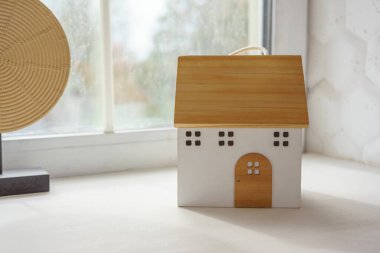 Ahşaptan yapılmış küçük dekoratif oyuncak evi parlak pencere pervazında duruyor. Ev dekorasyonu, çocuk odası için iç tasarım ayrıntıları.. 