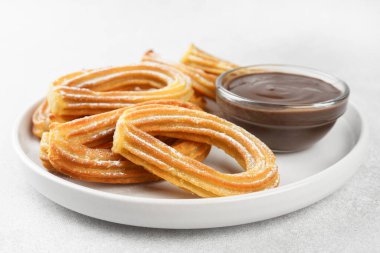 Geleneksel İspanyol tatlı churros, beyaz arka planda pudra şekeri ve çikolata sosuyla tozlanmış kızarmış hamur tatlısı. Sokak yemeği, tatlı atıştırmalık, ev yapımı tatlı. Üst görünüm, alanı kopyala
