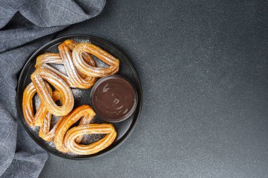 Geleneksel İspanyol tatlıları, pudra şekerli hamur tatlısı ve siyah arka planda çikolata sosu. Sokak yemeği, tatlı atıştırmalık, ev yapımı tatlı. Üst görünüm, alanı kopyala