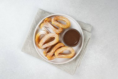 Geleneksel İspanyol tatlı churros, beyaz arka planda pudra şekeri ve çikolata sosuyla tozlanmış kızarmış hamur tatlısı. Sokak yemeği, tatlı atıştırmalık, ev yapımı tatlı. Üst görünüm, alanı kopyala
