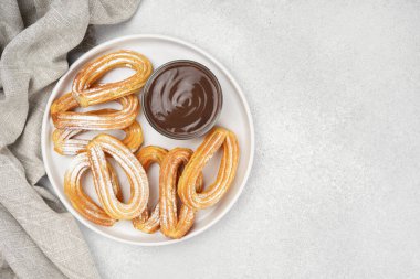 Geleneksel İspanyol tatlı churros, beyaz arka planda pudra şekeri ve çikolata sosuyla tozlanmış kızarmış hamur tatlısı. Sokak yemeği, tatlı atıştırmalık, ev yapımı tatlı. Üst görünüm, alanı kopyala