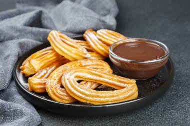 Geleneksel İspanyol tatlıları, pudra şekerli hamur tatlısı ve siyah arka planda çikolata sosu. Sokak yemeği, tatlı atıştırmalık, ev yapımı tatlı..