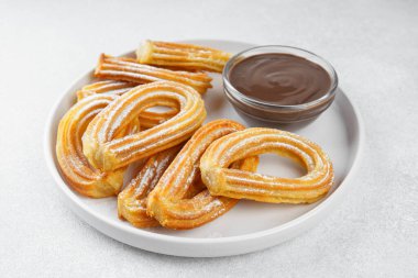 Geleneksel İspanyol tatlı churros, beyaz arka planda pudra şekeri ve çikolata sosuyla tozlanmış kızarmış hamur tatlısı. Sokak yemeği, tatlı atıştırmalık, ev yapımı tatlı. Üst görünüm, alanı kopyala