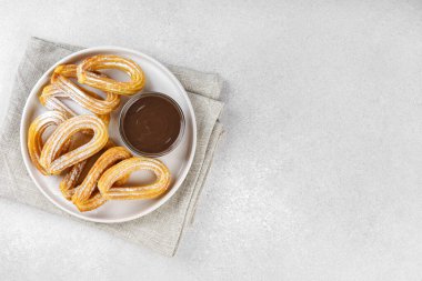 Geleneksel İspanyol tatlı churros, beyaz arka planda pudra şekeri ve çikolata sosuyla tozlanmış kızarmış hamur tatlısı. Sokak yemeği, tatlı atıştırmalık, ev yapımı tatlı. Üst görünüm, alanı kopyala