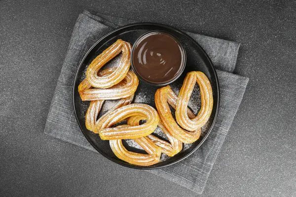 Geleneksel İspanyol tatlıları, pudra şekerli hamur tatlısı ve siyah arka planda çikolata sosu. Sokak yemeği, tatlı atıştırmalık, ev yapımı tatlı. Üst manzara, düz uzanma