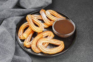 Geleneksel İspanyol tatlıları, pudra şekerli hamur tatlısı ve siyah arka planda çikolata sosu. Sokak yemeği, tatlı atıştırmalık, ev yapımı tatlı..