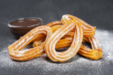 Geleneksel İspanyol tatlıları, pudra şekerli hamur tatlısı ve siyah arka planda çikolata sosu. Sokak yemeği, tatlı atıştırmalık, ev yapımı tatlı..