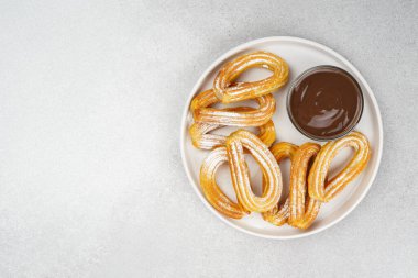 Geleneksel İspanyol tatlı churros, beyaz arka planda pudra şekeri ve çikolata sosuyla tozlanmış kızarmış hamur tatlısı. Sokak yemeği, tatlı atıştırmalık, ev yapımı tatlı. Üst görünüm, alanı kopyala