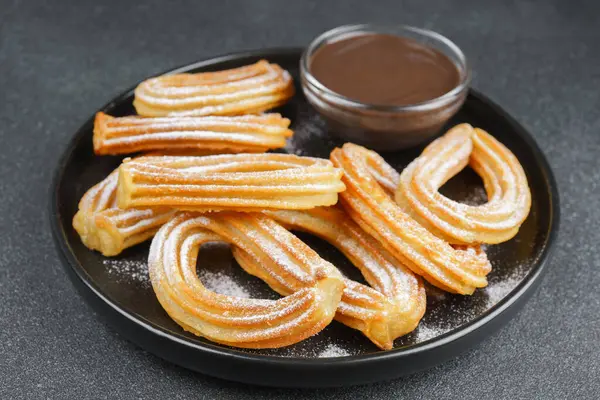 Geleneksel İspanyol tatlıları, pudra şekerli hamur tatlısı ve siyah arka planda çikolata sosu. Sokak yemeği, tatlı atıştırmalık, ev yapımı tatlı..