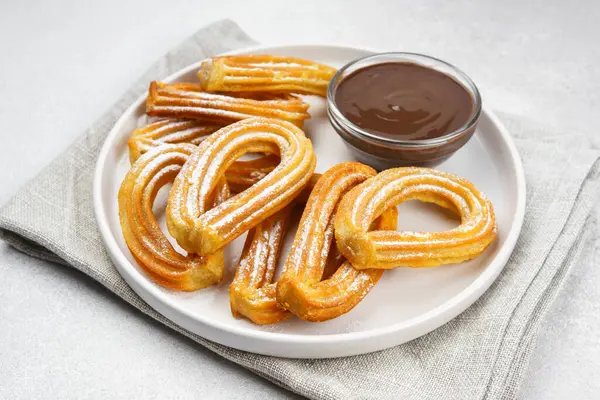 Geleneksel İspanyol tatlı churros, beyaz arka planda pudra şekeri ve çikolata sosuyla tozlanmış kızarmış hamur tatlısı. Sokak yemeği, tatlı atıştırmalık, ev yapımı tatlı. Üst görünüm, alanı kopyala