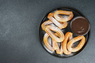 Geleneksel İspanyol tatlıları, pudra şekerli hamur tatlısı ve siyah arka planda çikolata sosu. Sokak yemeği, tatlı atıştırmalık, ev yapımı tatlı. Üst görünüm, alanı kopyala