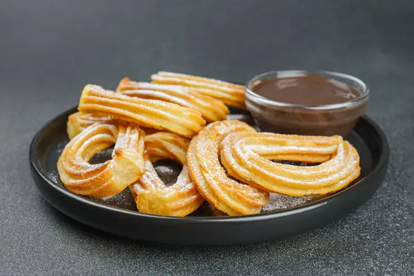 Geleneksel İspanyol tatlıları, pudra şekerli hamur tatlısı ve siyah arka planda çikolata sosu. Sokak yemeği, tatlı atıştırmalık, ev yapımı tatlı..