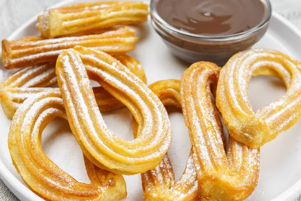 Geleneksel İspanyol tatlı churros, toz şeker ve çikolatalı sosis tozlu hamur tatlısı, yakın plan, beyaz arka plan. Sokak yemeği, tatlı atıştırmalık, ev yapımı tatlı.