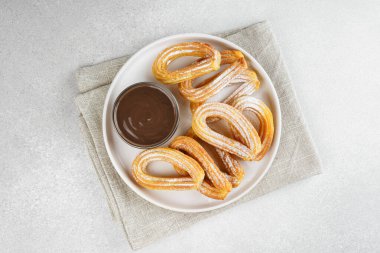 Geleneksel İspanyol tatlı churros, beyaz arka planda pudra şekeri ve çikolata sosuyla tozlanmış kızarmış hamur tatlısı. Sokak yemeği, tatlı atıştırmalık, ev yapımı tatlı. Üst görünüm, alanı kopyala