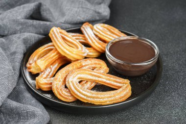 Geleneksel İspanyol tatlıları, pudra şekerli hamur tatlısı ve siyah arka planda çikolata sosu. Sokak yemeği, tatlı atıştırmalık, ev yapımı tatlı..