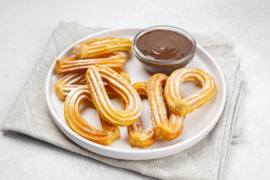 Geleneksel İspanyol tatlı churros, toz şeker ve çikolatalı sosis tozlu hamur tatlısı, yakın plan, beyaz arka plan. Sokak yemeği, tatlı atıştırmalık, ev yapımı tatlı.