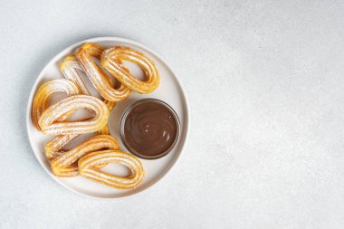 Geleneksel İspanyol tatlı churros, beyaz arka planda pudra şekeri ve çikolata sosuyla tozlanmış kızarmış hamur tatlısı. Sokak yemeği, tatlı atıştırmalık, ev yapımı tatlı. Üst görünüm, alanı kopyala