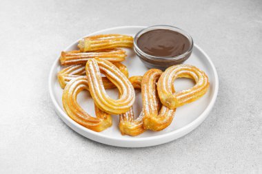 Geleneksel İspanyol tatlı churros, beyaz arka planda pudra şekeri ve çikolata sosuyla tozlanmış kızarmış hamur tatlısı. Sokak yemeği, tatlı atıştırmalık, ev yapımı tatlı. Üst görünüm, alanı kopyala