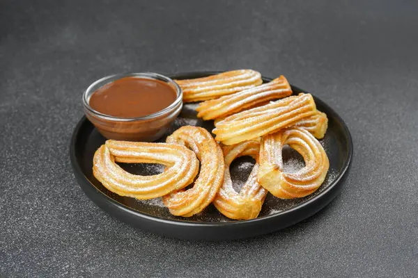 Geleneksel İspanyol tatlıları, pudra şekerli hamur tatlısı ve siyah arka planda çikolata sosu. Sokak yemeği, tatlı atıştırmalık, ev yapımı tatlı..