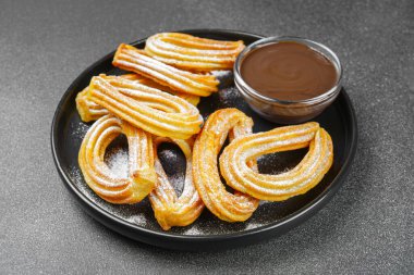 Geleneksel İspanyol tatlıları, pudra şekerli hamur tatlısı ve siyah arka planda çikolata sosu. Sokak yemeği, tatlı atıştırmalık, ev yapımı tatlı..