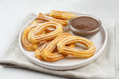 Geleneksel İspanyol tatlı churros, beyaz arka planda pudra şekeri ve çikolata sosuyla tozlanmış kızarmış hamur tatlısı. Sokak yemeği, tatlı atıştırmalık, ev yapımı tatlı. Üst görünüm, alanı kopyala