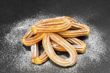 Geleneksel İspanyol tatlıları, siyah arka planda pudra şekerli kızarmış hamur tatlısı. Sokak yemeği, tatlı atıştırmalık, ev yapımı tatlı..