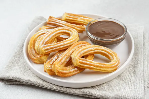 Geleneksel İspanyol tatlı churros, beyaz arka planda pudra şekeri ve çikolata sosuyla tozlanmış kızarmış hamur tatlısı. Sokak yemeği, tatlı atıştırmalık, ev yapımı tatlı. Üst görünüm, alanı kopyala
