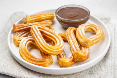 Geleneksel İspanyol tatlı churros, beyaz arka planda pudra şekeri ve çikolata sosuyla tozlanmış kızarmış hamur tatlısı. Sokak yemeği, tatlı atıştırmalık, ev yapımı tatlı. Üst görünüm, alanı kopyala