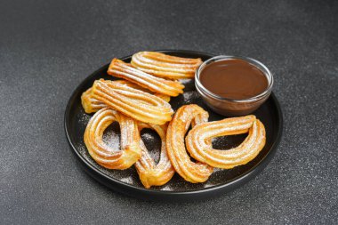 Geleneksel İspanyol tatlıları, pudra şekerli hamur tatlısı ve siyah arka planda çikolata sosu. Sokak yemeği, tatlı atıştırmalık, ev yapımı tatlı..