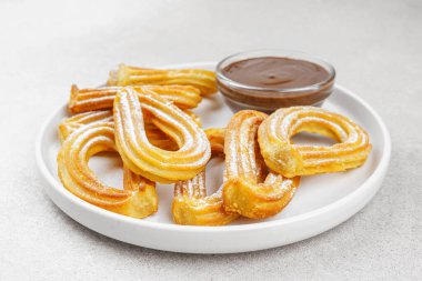 Geleneksel İspanyol tatlı churros, beyaz arka planda pudra şekeri ve çikolata sosuyla tozlanmış kızarmış hamur tatlısı. Sokak yemeği, tatlı atıştırmalık, ev yapımı tatlı. Üst görünüm, alanı kopyala