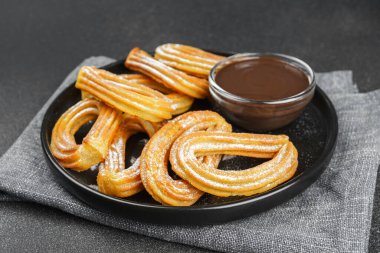 Geleneksel İspanyol tatlıları, pudra şekerli hamur tatlısı ve siyah arka planda çikolata sosu. Sokak yemeği, tatlı atıştırmalık, ev yapımı tatlı..