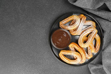 Geleneksel İspanyol tatlıları, pudra şekerli hamur tatlısı ve siyah arka planda çikolata sosu. Sokak yemeği, tatlı atıştırmalık, ev yapımı tatlı. Üst görünüm, alanı kopyala